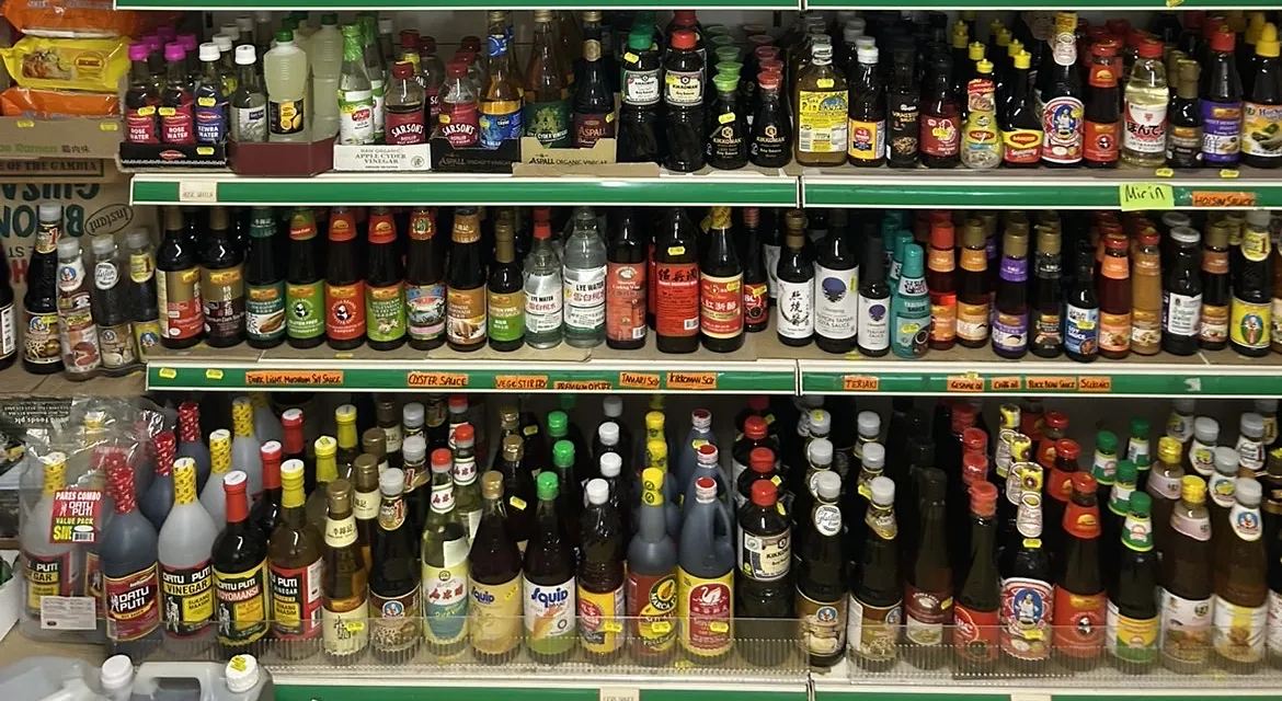 Three long shelves of soy, oyster, fish and chilli sauces in glass bottles