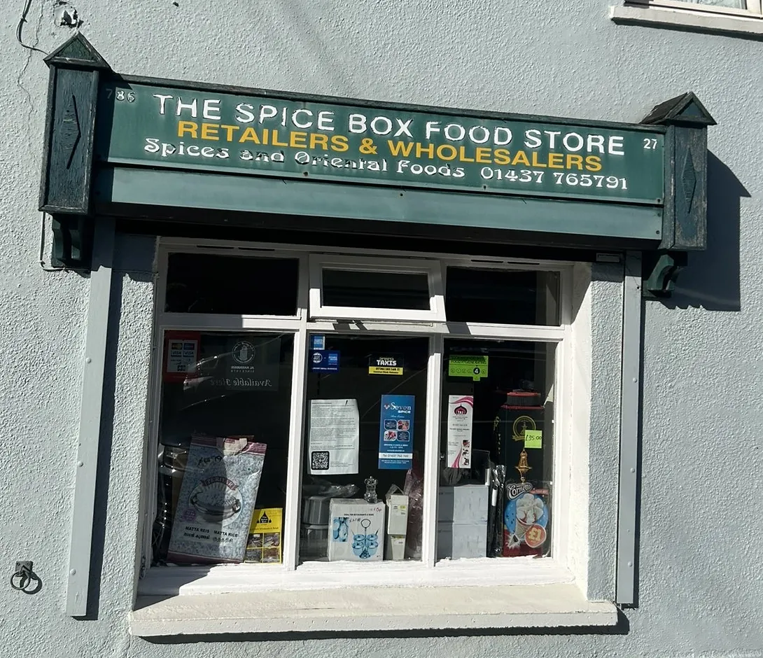 The Spice Box shopfront on Dew Street: a dark green sign reading The Spice Box Food Store, Retailers and Wholesalers, above a white bay window